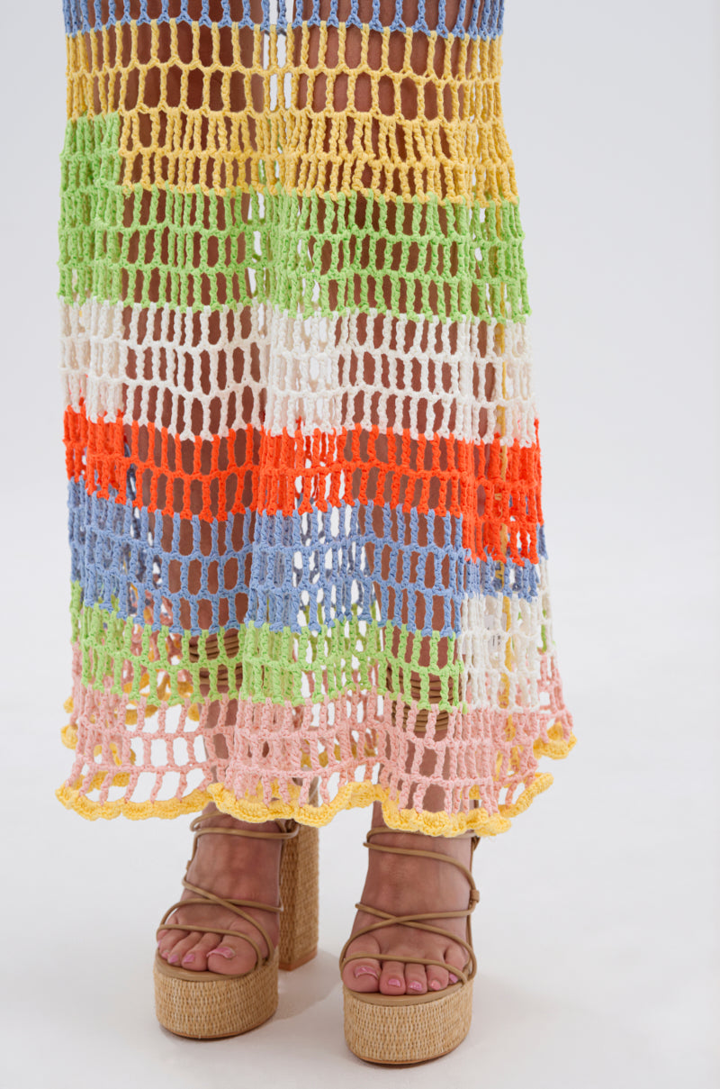 Wearing tan platform sandals, a person stands on a white surface displaying the colorful stripes of their BEACHIN IT CROCHET BEADED MAXI DRESS, visible from mid-calf down.