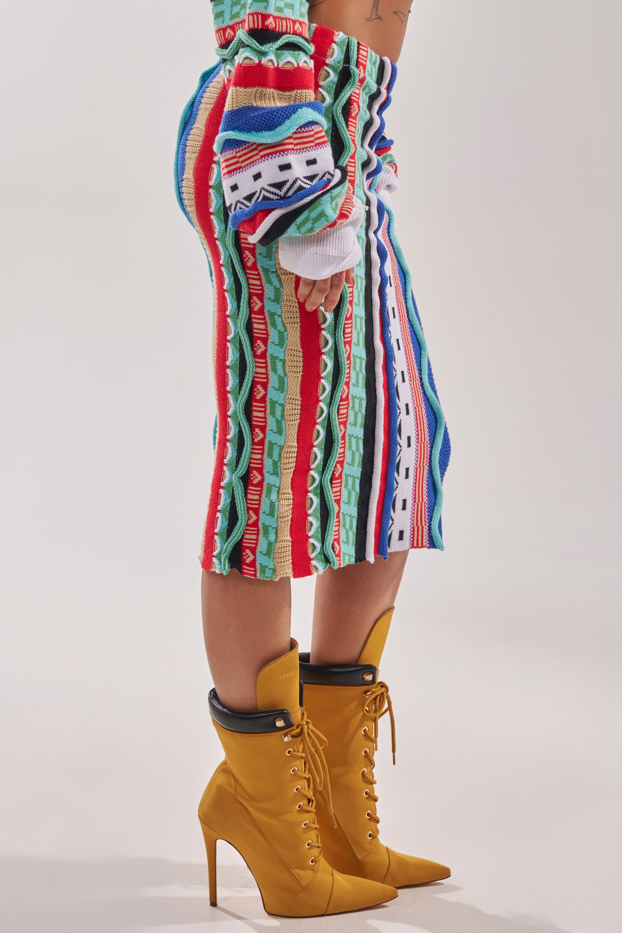 A person wears the FEELING THE VIBES MAXI SKIRT and matching top with mustard yellow high-heeled lace-up boots, standing against a plain light background. 3