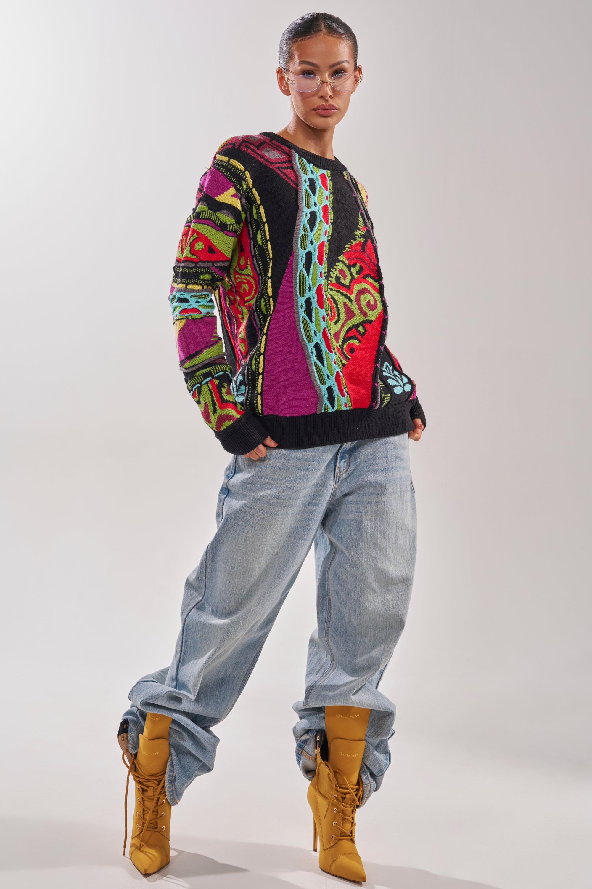 A person wears the GET GROOVY SWEATER, paired with loose light blue jeans, tan lace-up heeled boots, and clear glasses, standing confidently against a plain light background. 5