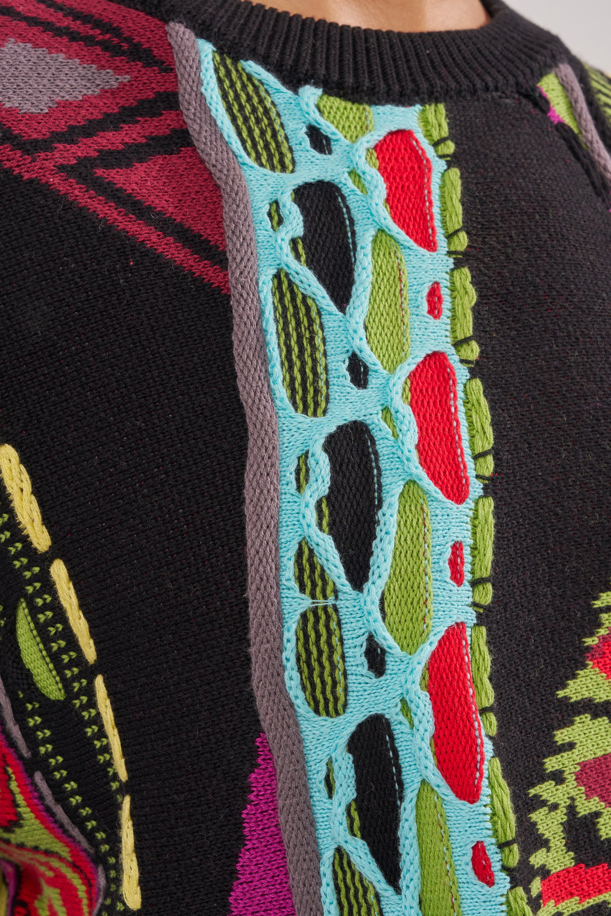 Close-up of the GET GROOVY SWEATER, showcasing its colorful patchwork design in red, green, yellow, and purple with raised blue stitching and open-knit sections. The unique knit texture and details are clearly visible. 7