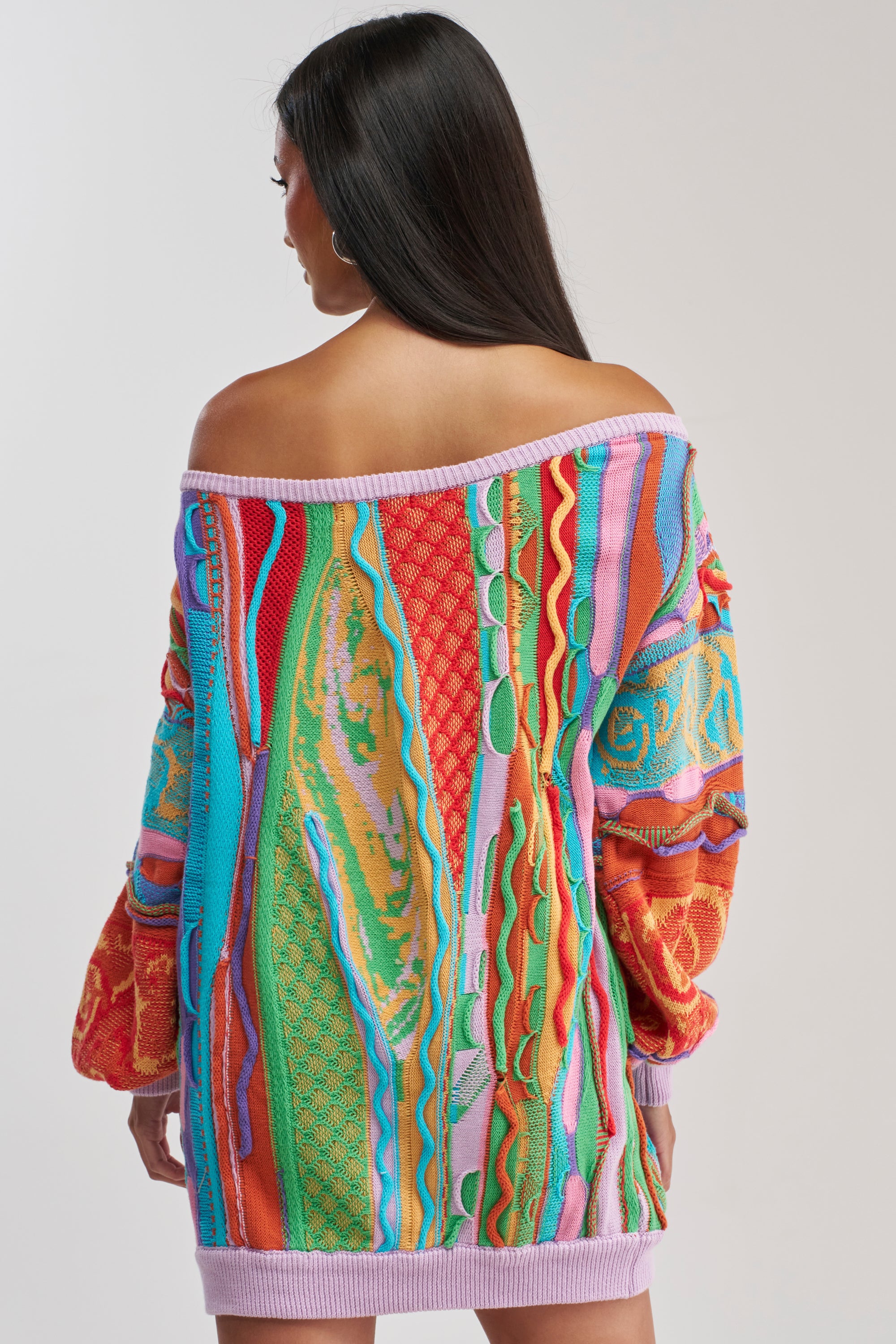 A woman with long dark hair, seen from behind, wears the CROWD FAVORITE SWEATER MINI DRESS—a colorful, off-the-shoulder sweater dress with wavy textured patterns and balloon sleeves, perfect for cozy winter layering with its loose fit.