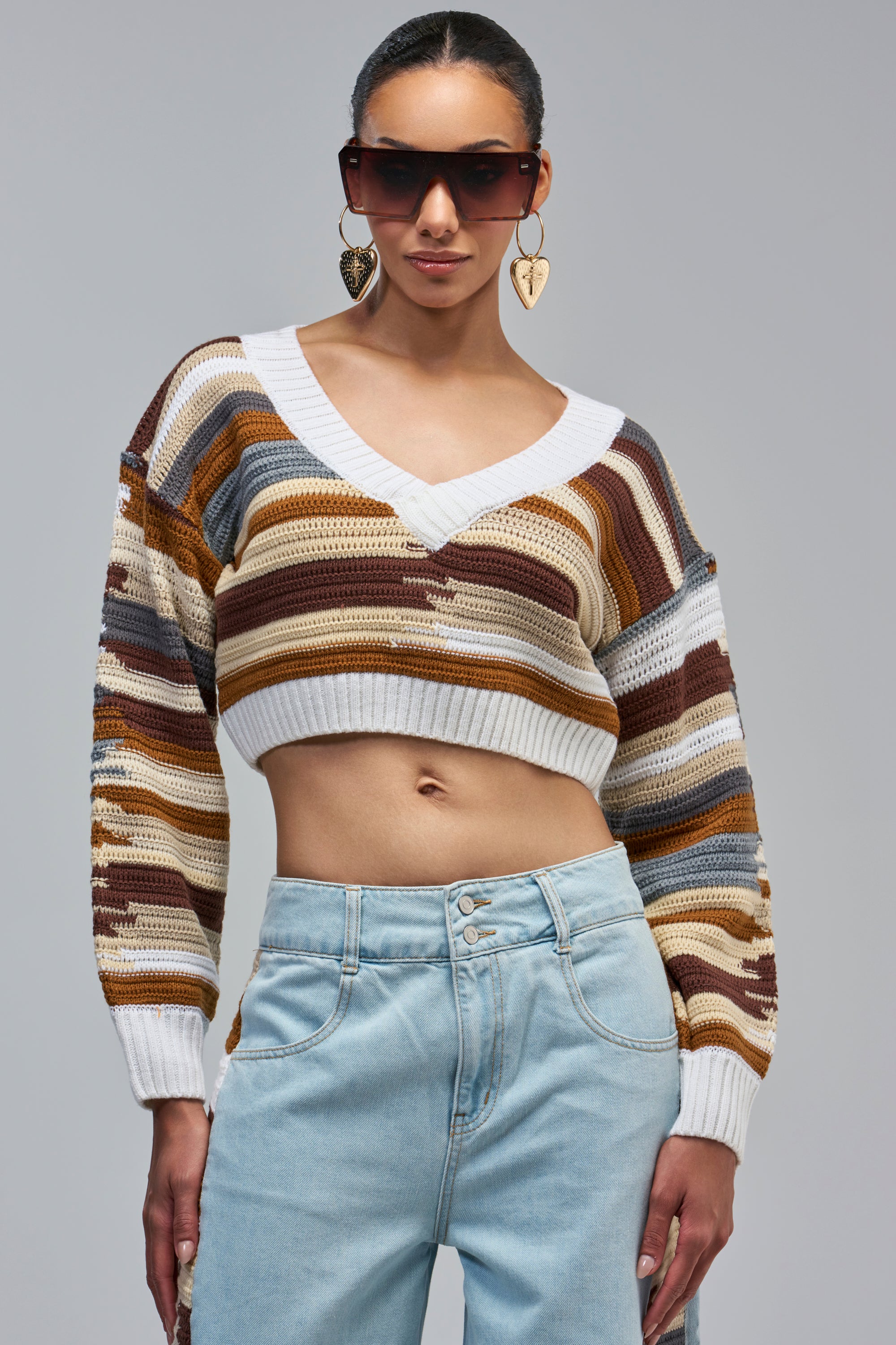 DRIVING ME INSANE CROCHET SWEATER, a cropped V-neck with horizontal stripes in shades of brown, tan, gray, and white, paired with light-wash denim jeans for a cozy fall outfit.