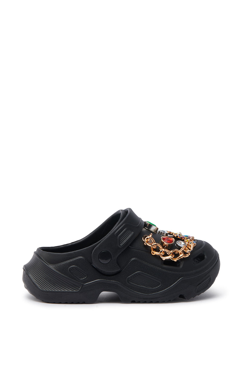 The AZALEA WANG EVERETT BLACK MULTI STONE GOLD CHAIN FLAT is a black slip-on clog with rugged soles, a gold chain detail, and colorful stone embellishments across the upper.