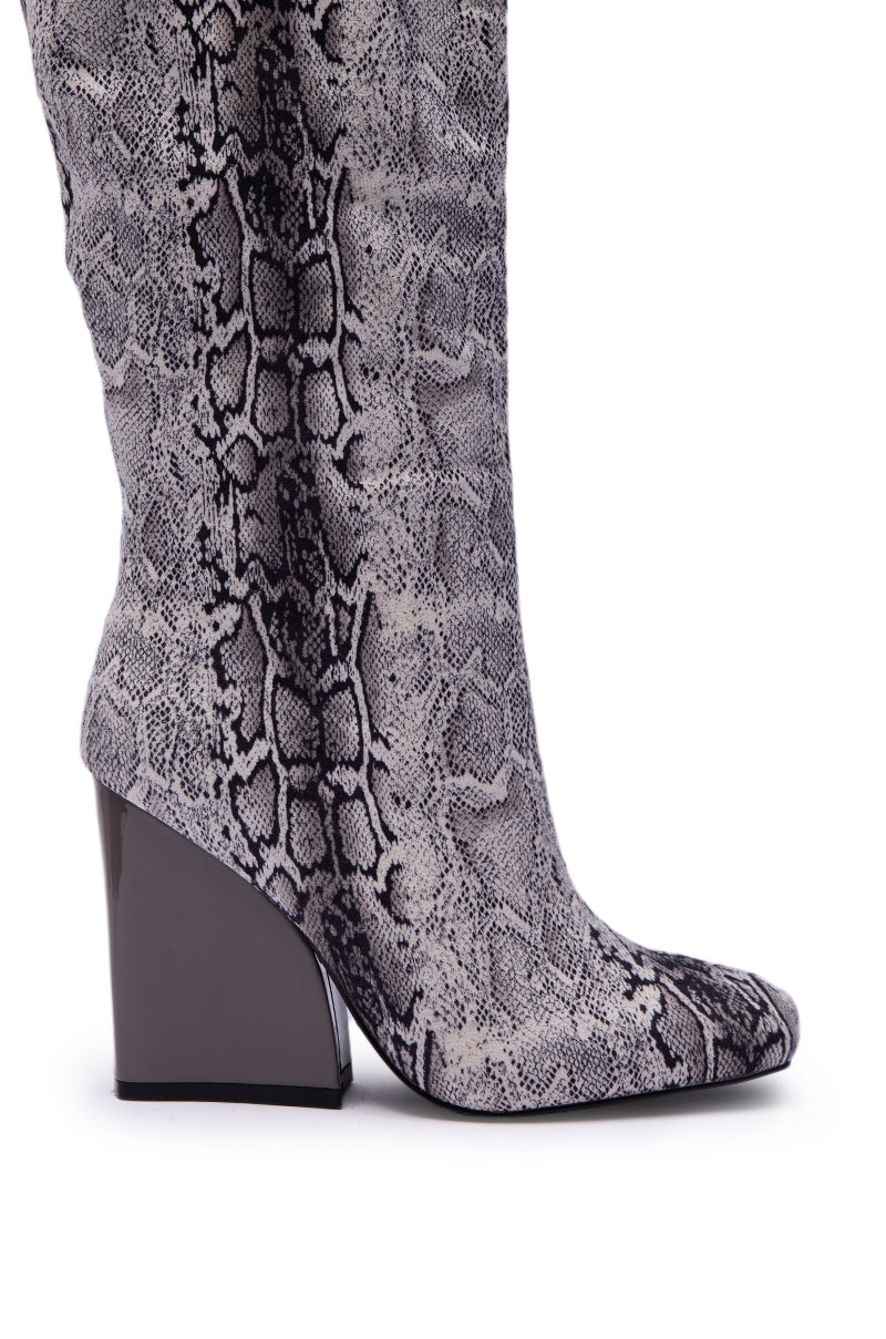 A close-up of the AZALEA WANG EVERGREEN GREY SNAKE PRINT CHUNKY HEEL BOOT, featuring knee-high styling with a bold grey snake print and a shiny, chunky block heel.
