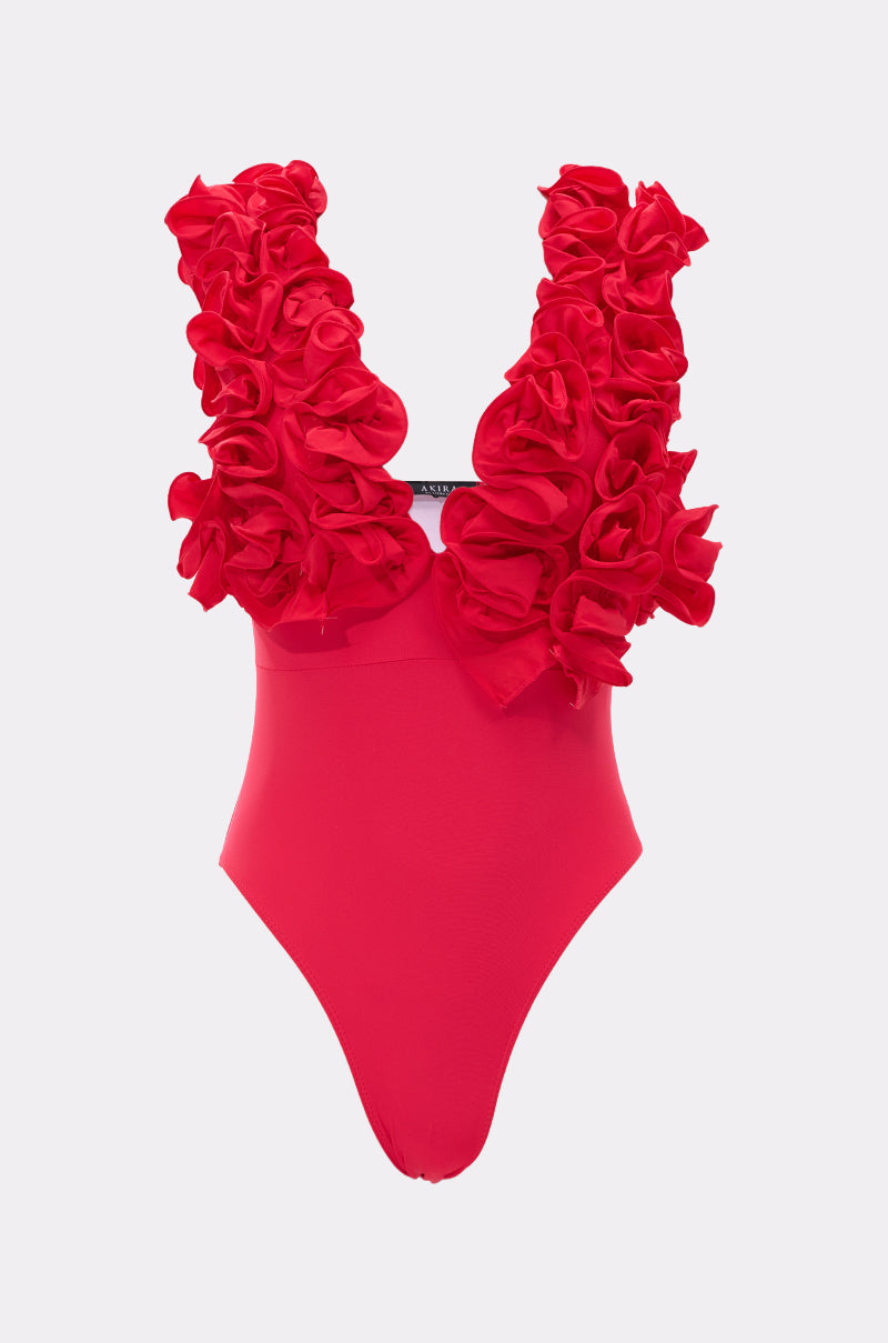 The LUXE LIFE RUFFLE SWIMSUIT is a vibrant pink one-piece featuring dramatic, layered ruffles on thick shoulder straps and a plunging neckline, showcased against a plain light gray background.