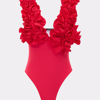 The LUXE LIFE RUFFLE SWIMSUIT is a vibrant pink one-piece featuring dramatic, layered ruffles on thick shoulder straps and a plunging neckline, showcased against a plain light gray background.