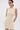 A woman models the FEELIN SWEET KNIT SWEATER DRESS WITH PEARLS, a sleeveless, cream-colored mini dress, standing against a plain white background with her hands behind her back and looking slightly to the side.