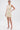 A woman poses against a white background in the FEELIN SWEET KNIT SWEATER DRESS WITH PEARLS, featuring pearl accents and a flattering fit. Her hair is pulled back, and she rests her hand on her hip while wearing clear high-heeled sandals.