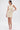A woman stands against a white background wearing the FEELIN SWEET Knit Sweater Dress with Pearls, a cream, curve-hugging mini dress with a textured finish, styled with white heeled sandals and her hair pulled back as she poses hand on hip.