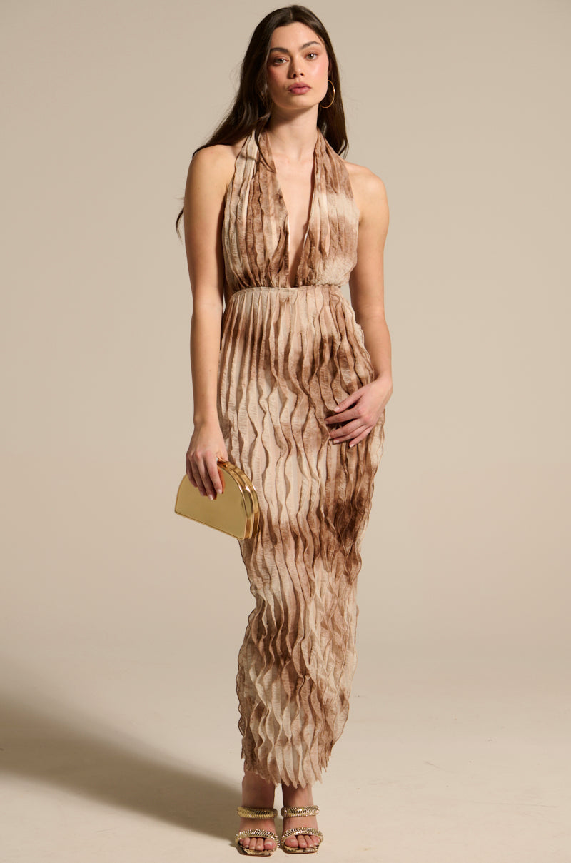 A woman wears the LOOK BUT DON'T TOUCH PRINTED MAXI DRESS, a sleeveless beige and brown tie-dye halter maxi, with long brown hair, gold hoop earrings, heeled sandals, and a small gold clutch against a light background.