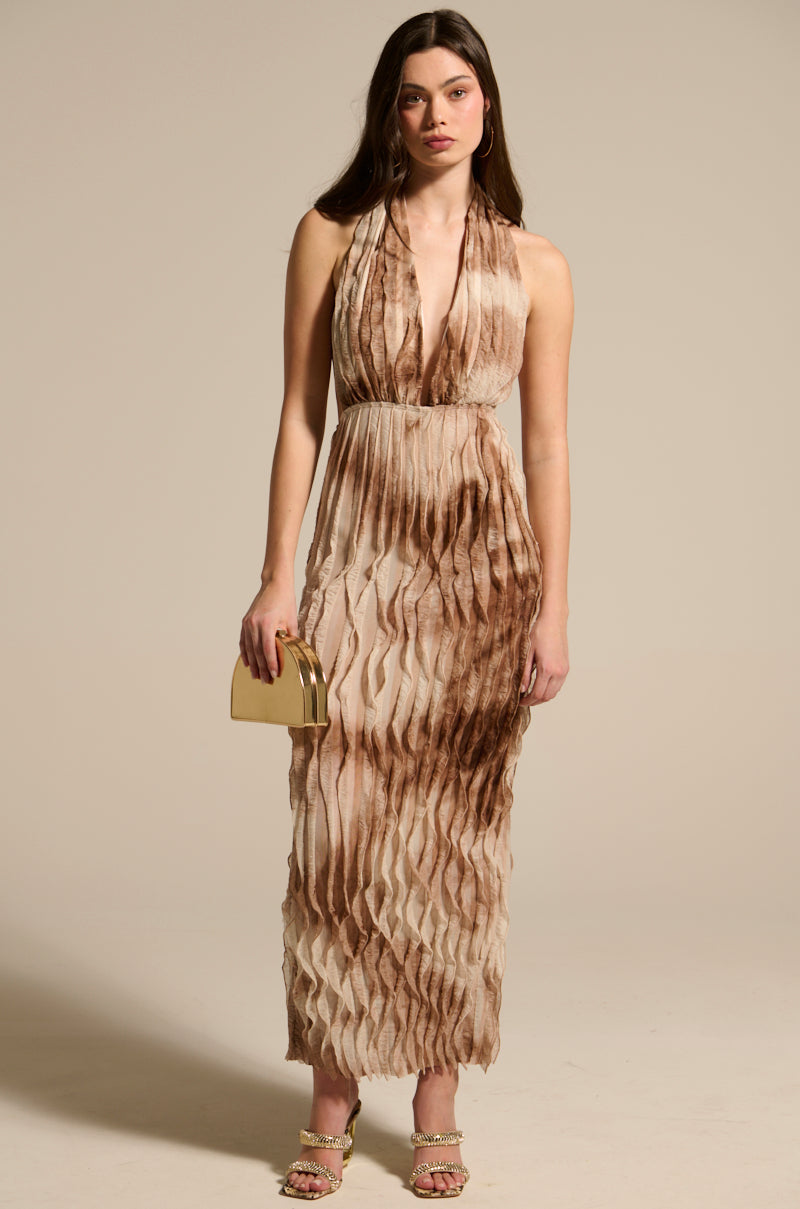 A woman faces forward in the LOOK BUT DON'T TOUCH PRINTED MAXI DRESS, a sleeveless, halter-neck, pleated maxi dress in brown and beige. She carries a small gold clutch and wears strappy heels against a plain background.