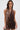 A woman with long brown hair and large hoop earrings wears the ALL ABOUT ME LEOPARD PRINT MINI DRESS, a sleeveless bodycon mini dress, as she stands against a white background holding a small item in her right hand.