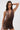 A woman poses confidently in the ALL ABOUT ME LEOPARD PRINT MINI DRESS—sleeveless, cowl neck, and bodycon fit—with large hoop earrings, one hand on her head, against a plain light background.