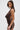 A woman with long brown hair stands sideways against a white background, looking at the camera and holding a clutch, wearing the ALL ABOUT ME LEOPARD PRINT MINI DRESS—a bodycon fit with an open-back design.