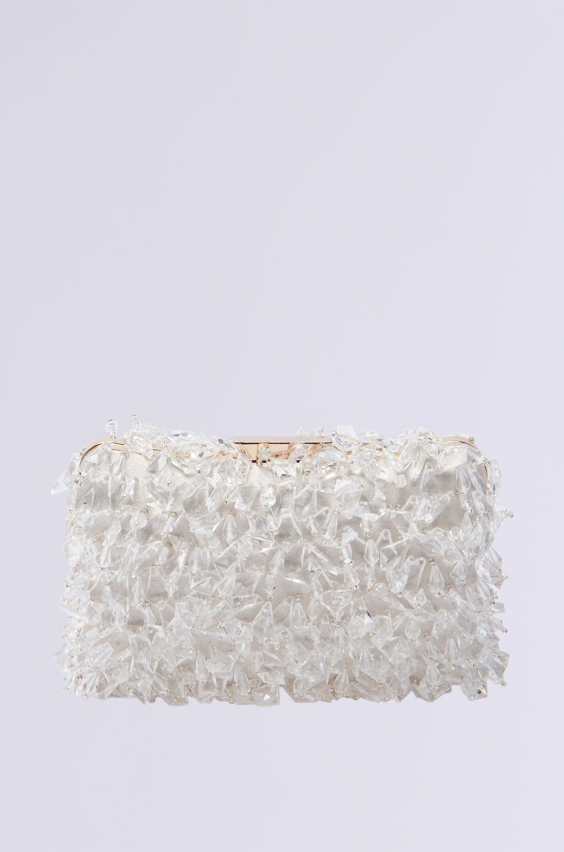 Introducing the CRYSTAL CLEAR DRIPPY CLUTCH, a rectangular purse adorned with clear jagged crystal-like beads over a light gray backdrop. This luxurious accessory features textured, sparkling elements to enhance any outfit with shimmering elegance.