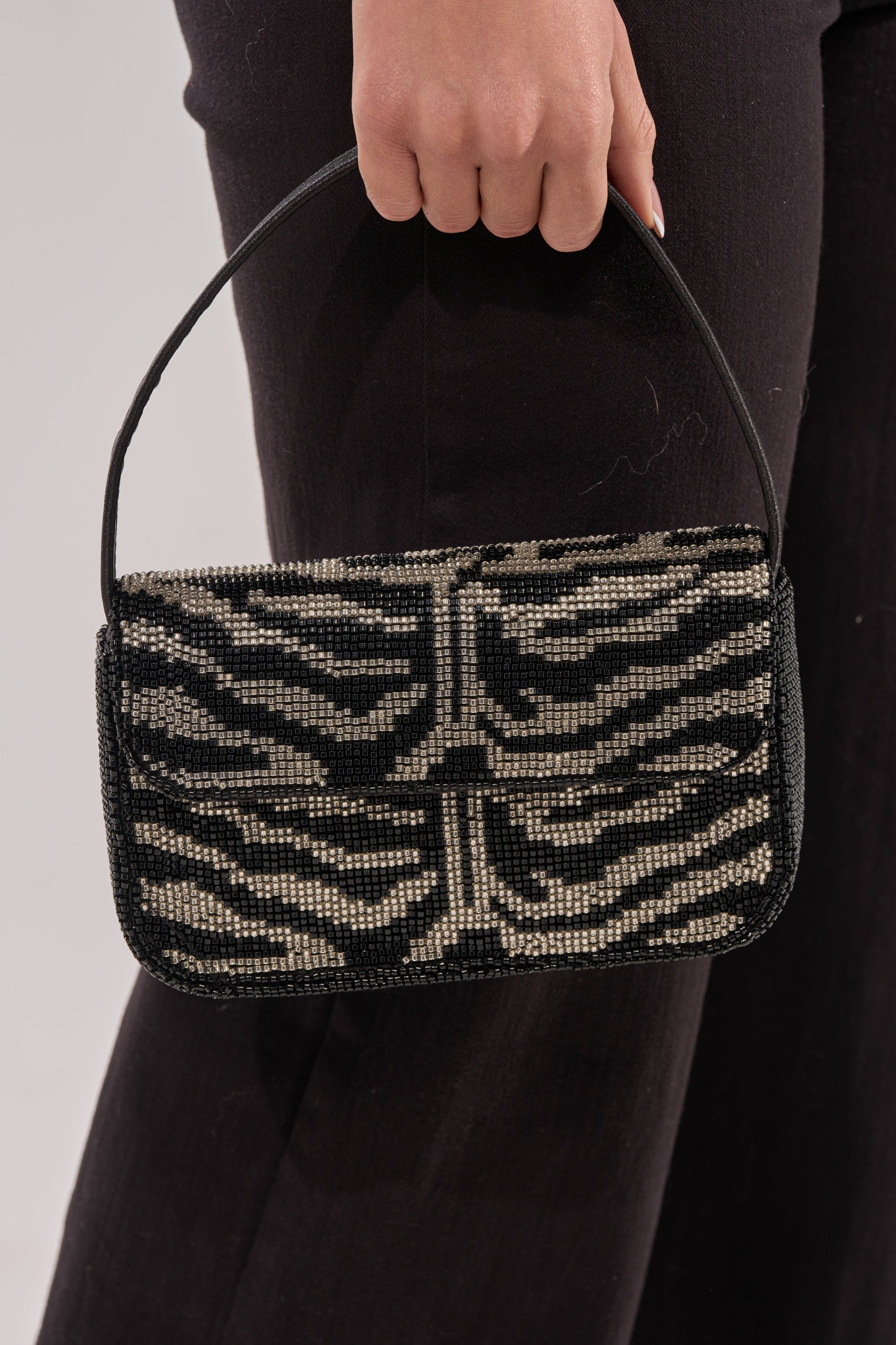 A person holding the VIVIANNE BEADED PURSE, a clutch with a black and silver beaded zebra pattern, paired with dark pants. 3