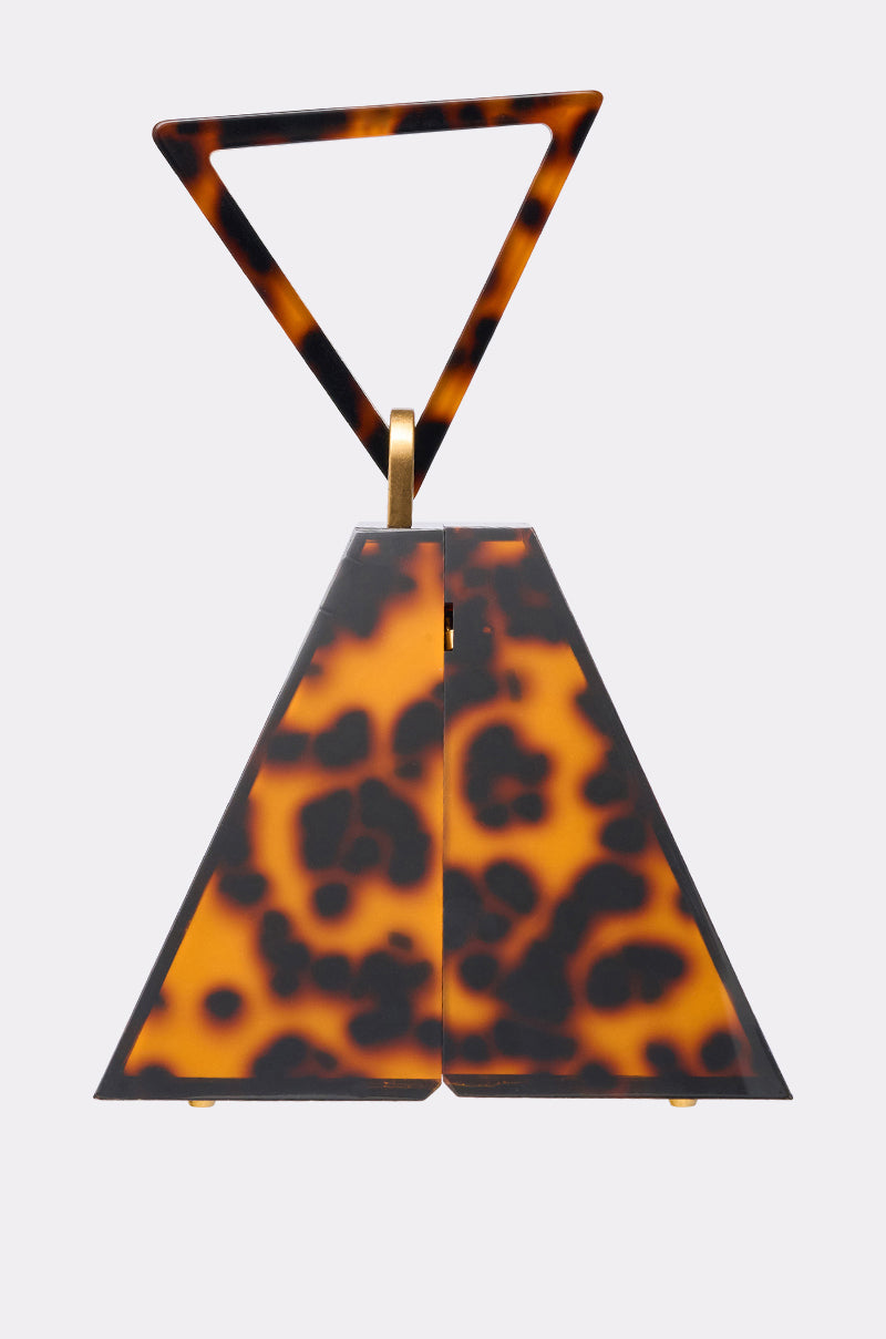 The TOP OF THE PYRAMID PURSE is a trapezoid-shaped handbag with a tortoiseshell pattern, matching triangular handle, and gold hinge accents, displayed on a plain light background. 1