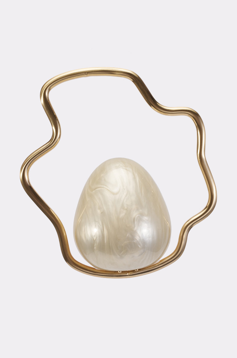 The GODDESS VIBES CLUTCH features a wavy, irregular gold metal frame encasing an ovular, marbled, egg-shaped clutch with a glossy off-white surface, presented against a plain white background.