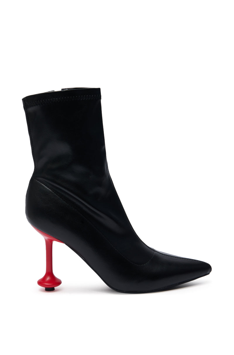 The AZALEA WANG FABBRI Black Bootie features a pointed toe, faux leather upper, and a distinctive red stiletto heel shaped like a chess pawn, all shown against a white background.