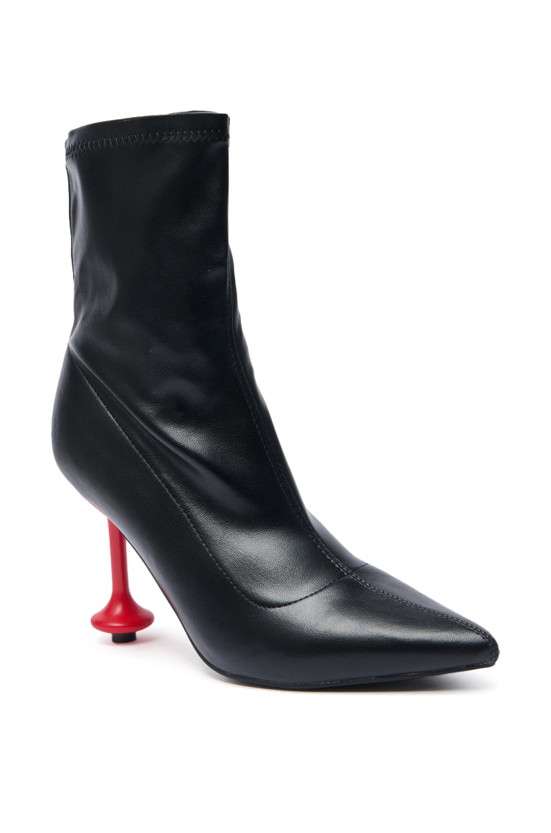 The AZALEA WANG FABBRI BLACK BOOTIE WITH RED HEEL features a sleek pointed toe, smooth leather texture, bold red stiletto heel, and high-fashion design.