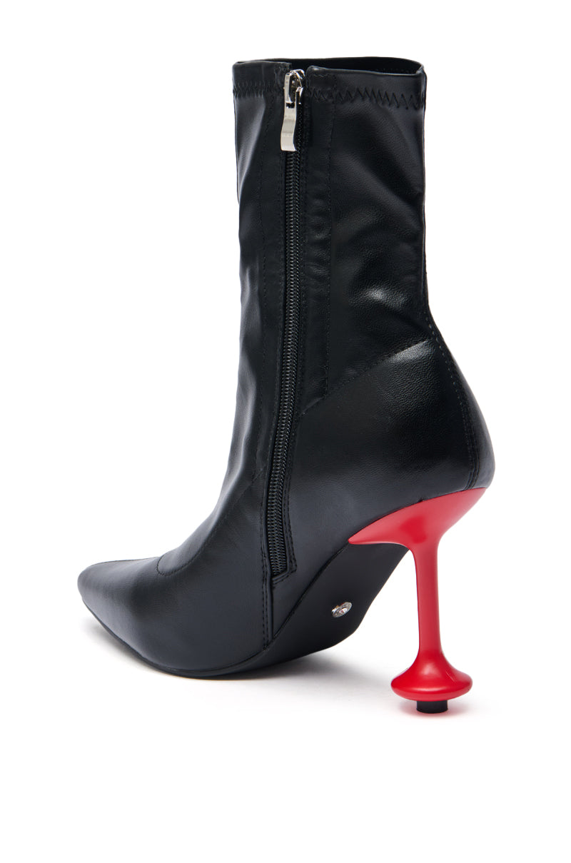 The AZALEA WANG FABBRI BLACK BOOTIE WITH RED HEEL features sleek faux leather, a side zipper, and a bold red stiletto heel inspired by a pawn chess piece.