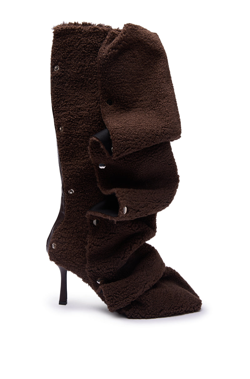 The AZALEA WANG FABIAN BROWN SHERPA FOLDED DETAIL BOOT is a single knee-high boot with a stiletto heel, textured brown fleece, layered ruffled folds, and a pointed toe, shown against a white background.