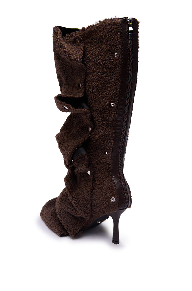 The AZALEA WANG FABIAN BROWN SHERPA FOLDED DETAIL BOOT is a knee-high stiletto boot in dark brown, fleece-like sherpa with ruffled details, snap buttons, and a side zipper, shown on a white background.