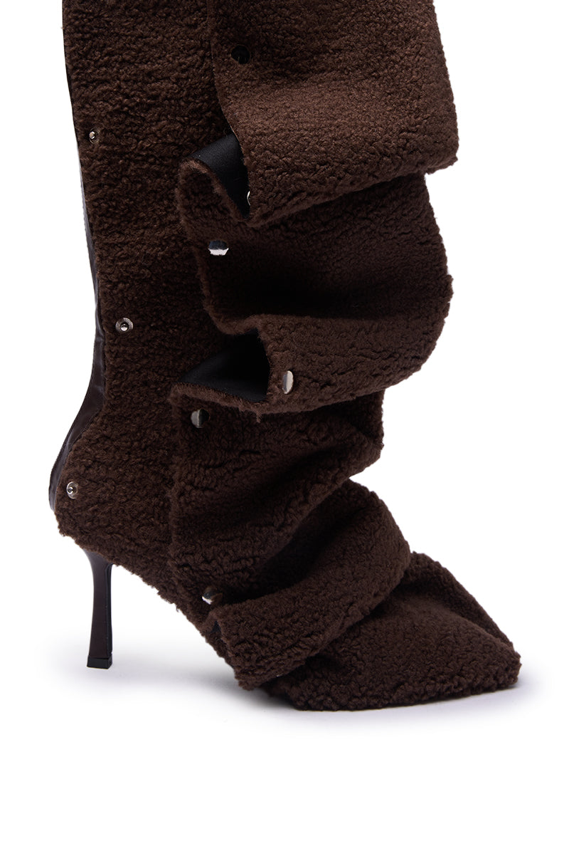 A close-up of the AZALEA WANG FABIAN BROWN SHERPA FOLDED DETAIL BOOT, a dark brown, textured shearling stiletto with a pointed toe and oversized layered flaps with snap buttons along the side.