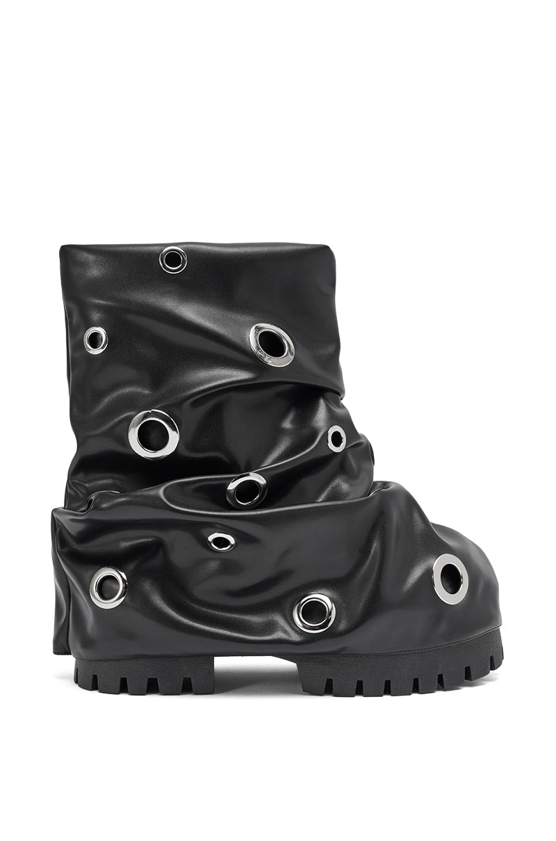 The AKIRA GOLD FABLE BLACK GROMMET EMBELLISHED FLAT BOOTIE is a black bootie featuring a chunky sole, draped slouched design, and multiple large silver grommets throughout.