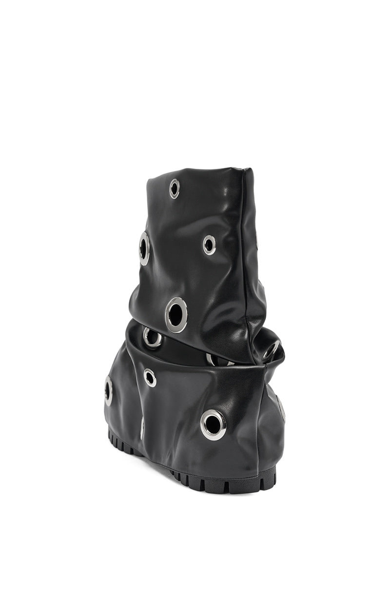 The AKIRA GOLD FABLE BLACK GROMMET EMBELLISHED FLAT BOOTIE showcases a slouchy black silhouette with large metal grommet accents and a chunky sole, shown in a side view against a white background.