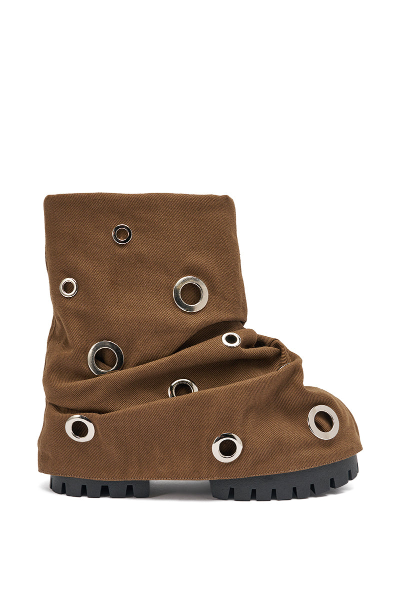 The AKIRA GOLD FABLE BROWN GROMMET EMBELLISHED FLAT BOOTIE features a slouchy brown design with multiple large silver eyelets and a chunky black treaded sole, shown against a white background. 3