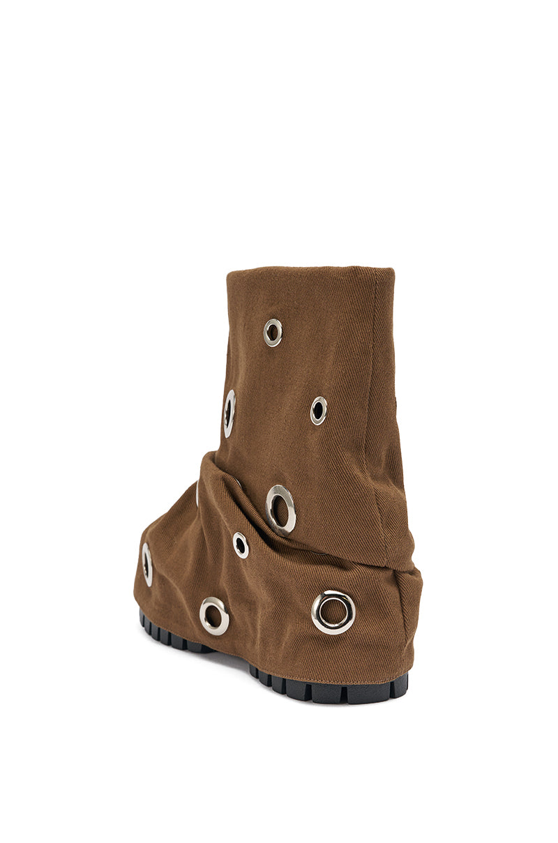 The AKIRA GOLD FABLE BROWN GROMMET EMBELLISHED FLAT BOOTIE features a slouchy, fabric-like texture and multiple silver grommets, shown in brown against a white background. 5