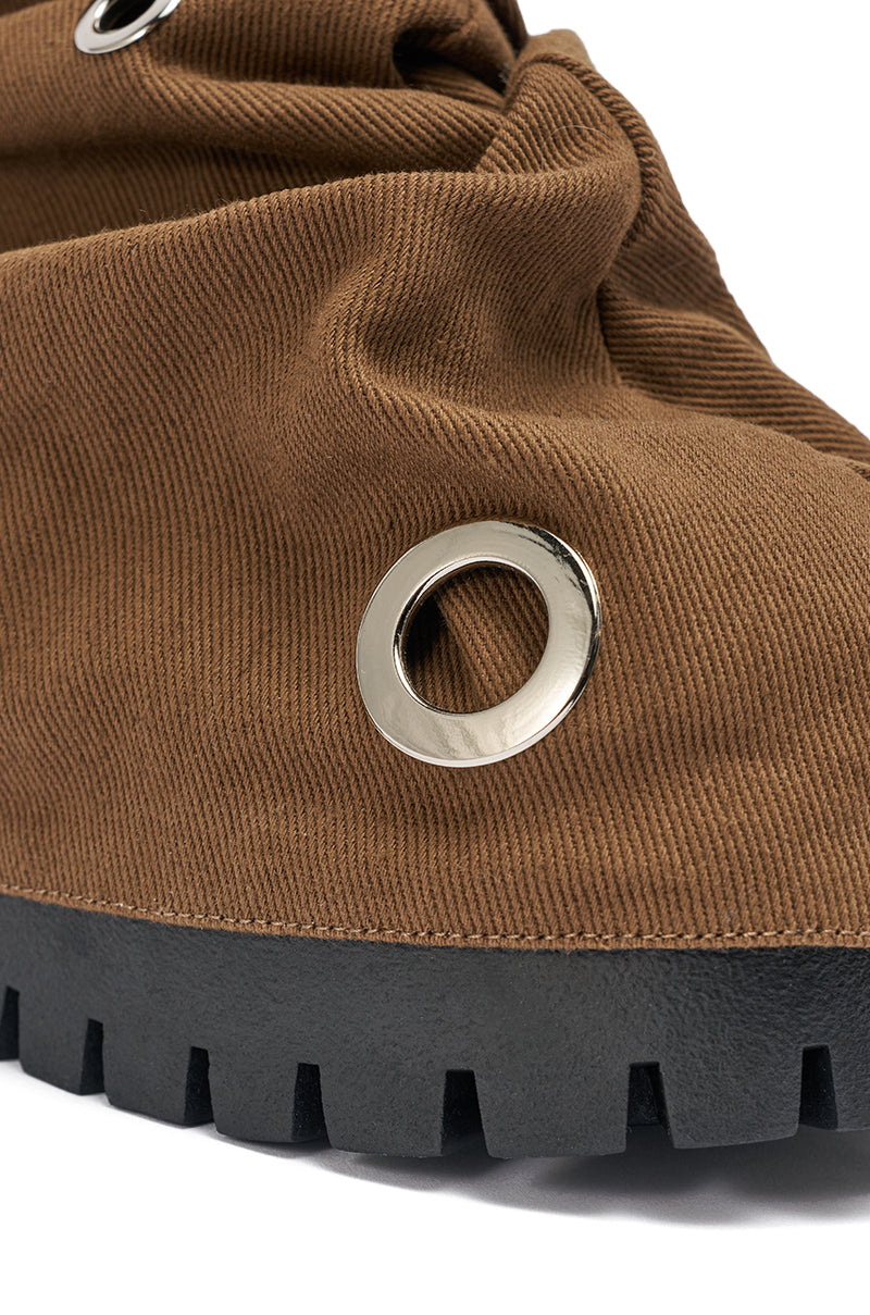 Close-up of the AKIRA GOLD FABLE BROWN GROMMET EMBELLISHED FLAT BOOTIE featuring large metallic eyelets and a thick, black, ridged lug sole on a white background. 6