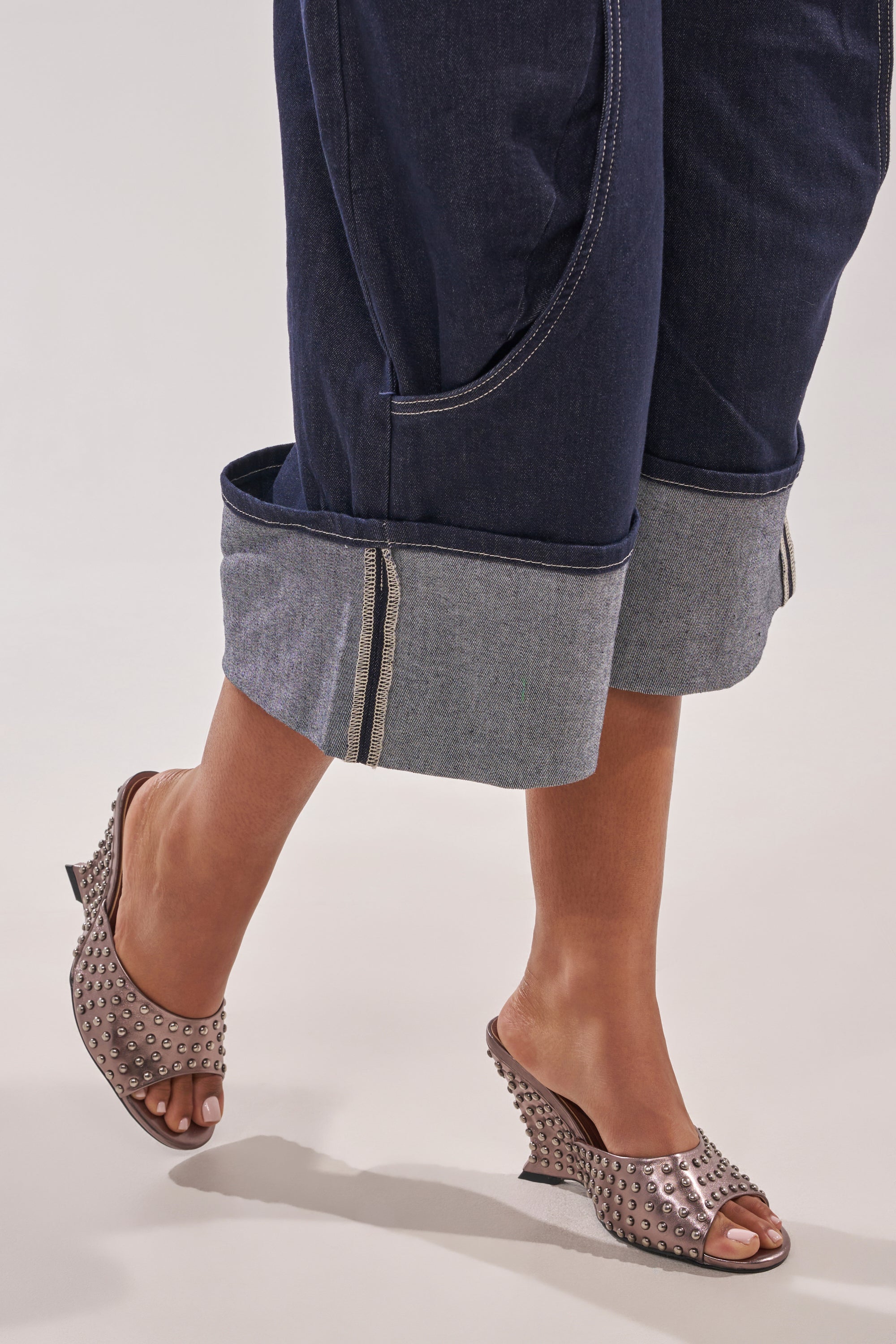 A person stands on tiptoe in dark cuffed denim pants and AZALEA WANG FABRON PEWTER EMBELLISHED WEDGE SANDALS against a light background. 3