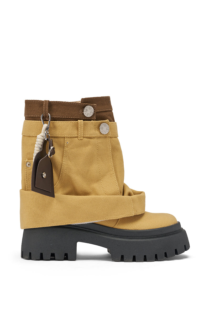 The AKIRA GOLD FAE TAN BOOTIE is a tan and brown ankle boot featuring a chunky lug heel, decorative wrap detail, silver buttons, and a small brown keychain attached near the top. 4