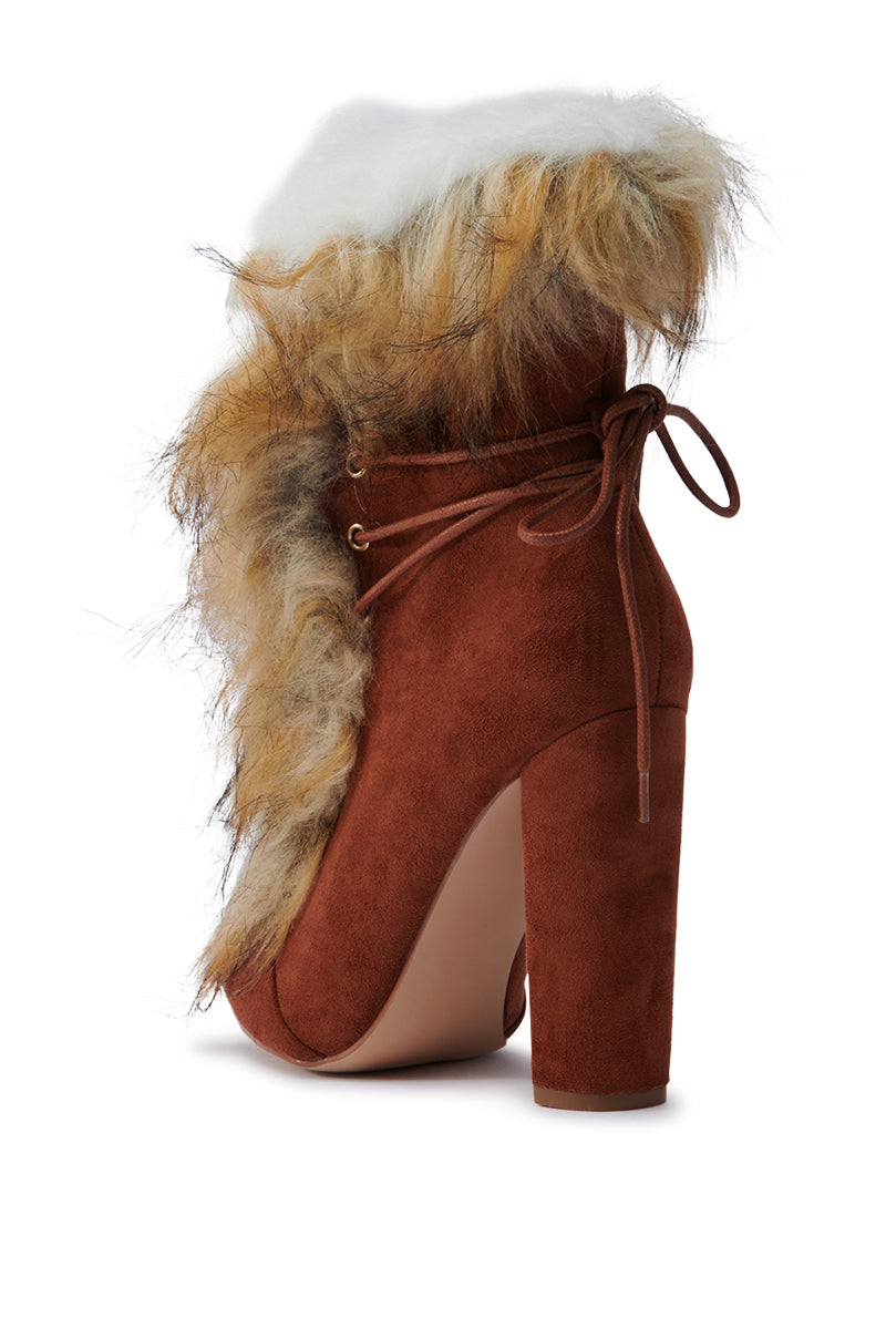 The FANCY TAN LACE UP CHUNKY BOOTIE WITH FUR is an exquisite high-heeled ankle boot featuring a reddish-brown faux suede finish and a chunky heel. The lace-up design pairs beautifully with the plush white and brown fur trim that drapes gracefully around the ankle.