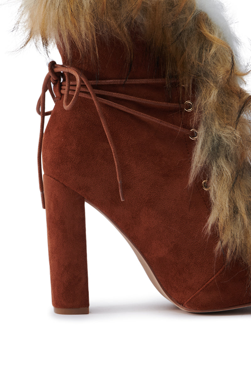 The FANCY TAN LACE UP CHUNKY BOOTIE WITH FUR showcases a faux suede construction, featuring a lace-up design and textured faux fur trim. Its chic style is complemented by a chunky heel that adds elegance to the sleek silhouette, while the fur offers a striking contrast.