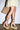 A person in a light yellow dress and AZALEA WANG FANTASA BROWN HALLOW PLATFORM WEDGE STRAPPY SANDALS with ankle ties and chain details, holding a woven straw tote bag, stands against a plain white background.