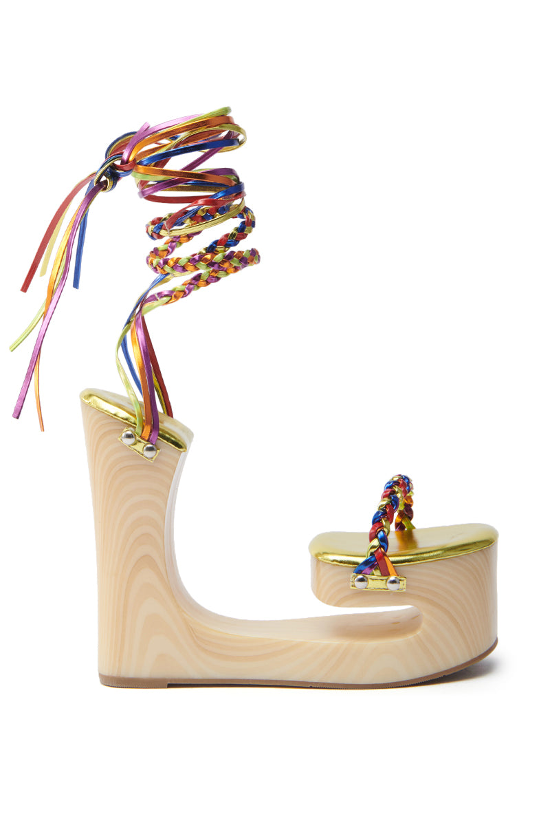 The AZALEA WANG FANTASA RAINBOW STRAPPY WEDGE SANDAL is a wooden sandal with a curved platform and no heel, featuring rainbow braided straps, ribbon ankle laces, and gold accents on the toe area.