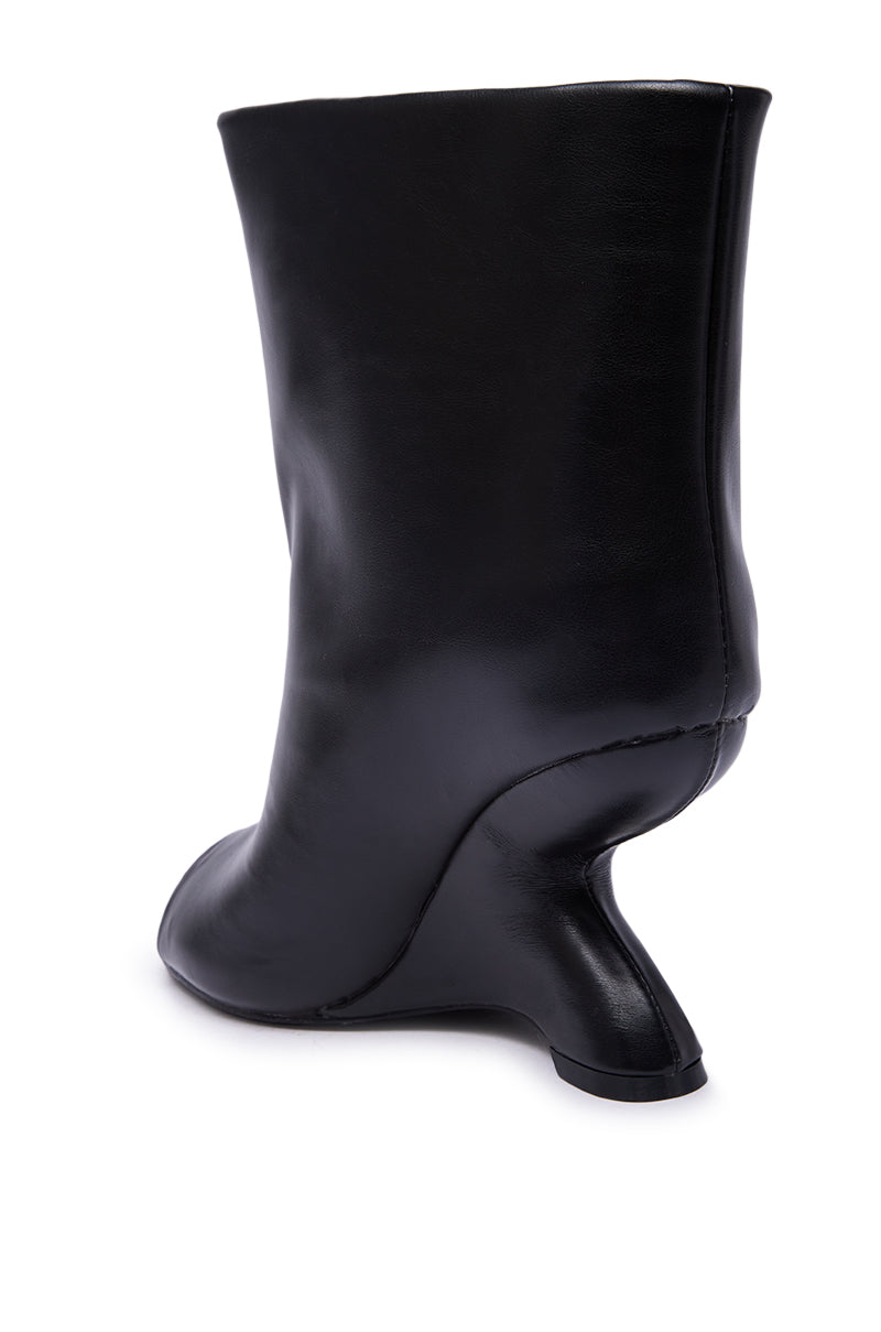 The AZALEA WANG FAOI Black Inverted Wedge Open-Toe Bootie features black faux leather and a unique, sculpted wedge heel that curves inward into the sole for a modern, avant-garde look. The image displays the bootie from a back-side angle.