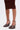 A person stands against a plain white background wearing a ruched brown skirt and the AZALEA WANG FASCIA CHOCOLATE WEDGE FRINGE SANDAL, featuring ankle straps and fringe detailing on the front.