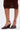 A person stands against a white background wearing a brown ruched skirt and the AZALEA WANG FASCIA CHOCOLATE WEDGE FRINGE SANDAL, crafted from faux leather with fringe details.