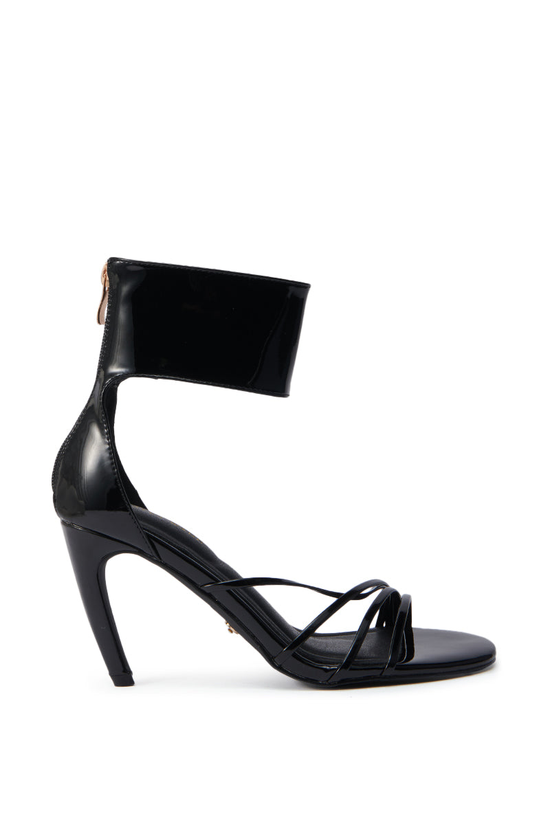The AZALEA WANG FAWZI Black Banana Heel Cuffed Sandal features a wide ankle strap, thin crisscross toe straps, back zipper, and comfort cushion insole. Shown in side profile on a white background. 2