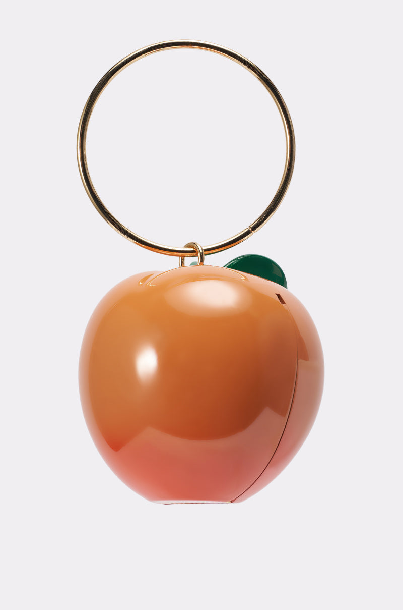 The FEELIN PEACHY BAG is a novelty handbag inspired by a peach keychain, featuring a shiny surface, large gold ring handle, and a small green leaf detail at the top. 3