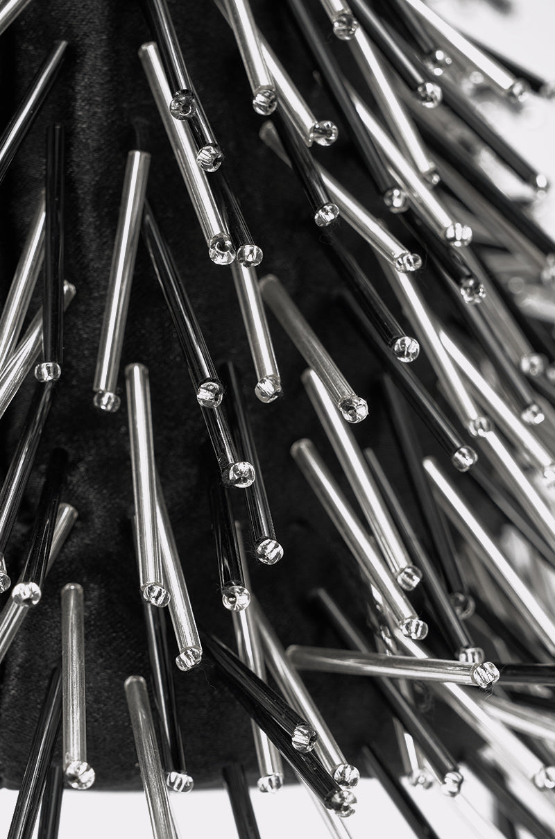 Close-up of silver and black metallic rods on a dark background, creating a spiky, textured look that resembles the TOUCH ME PURSE. This striking black and white image highlights the handbag's bold embellishments. 3