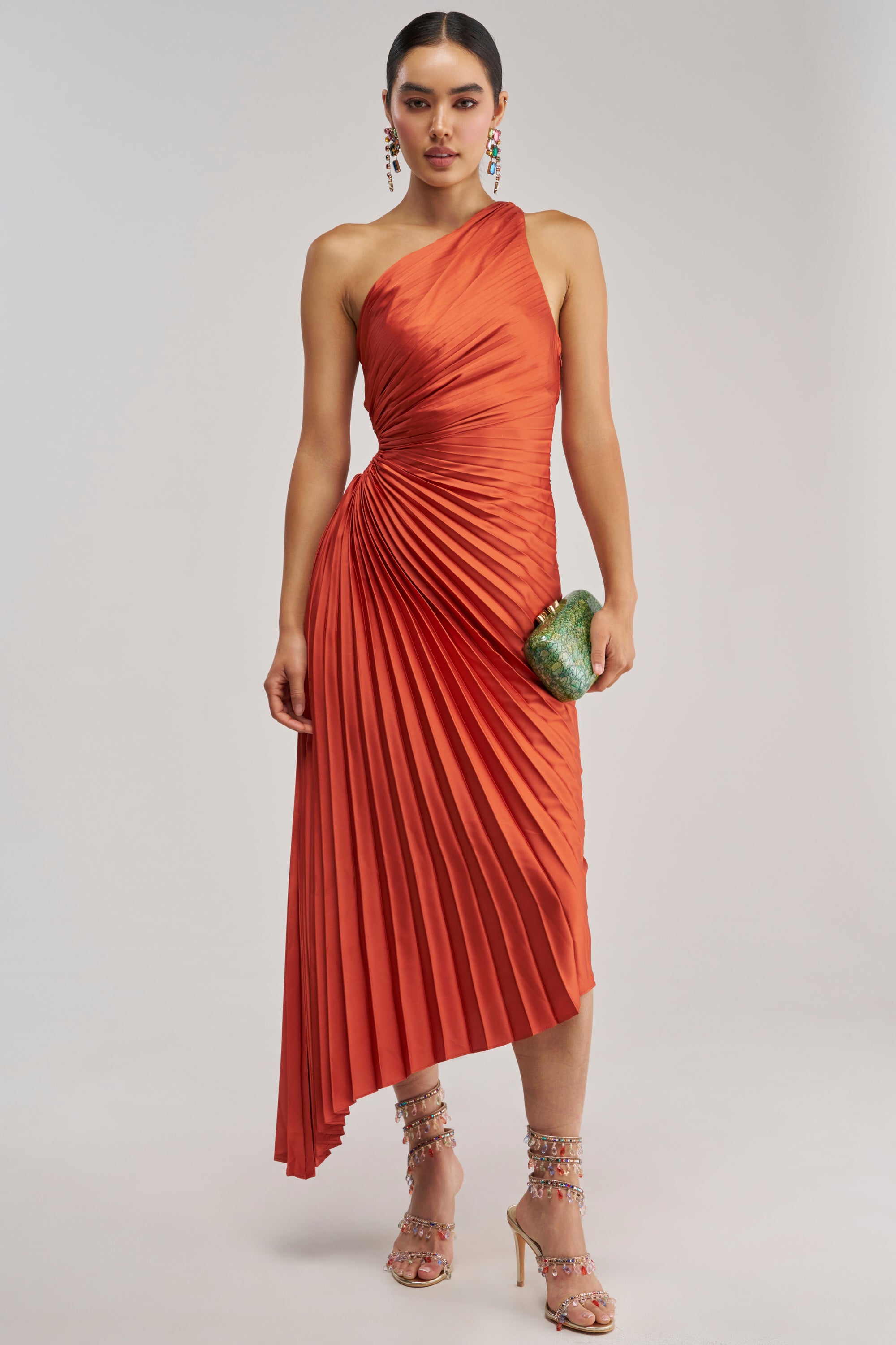 A woman in the MIDNIGHT MAVEN Sleeveless Maxi Dress in red holds a green clutch and wears embellished high-heeled sandals, posing against a plain light background—an elegant look perfect for any formal occasion.