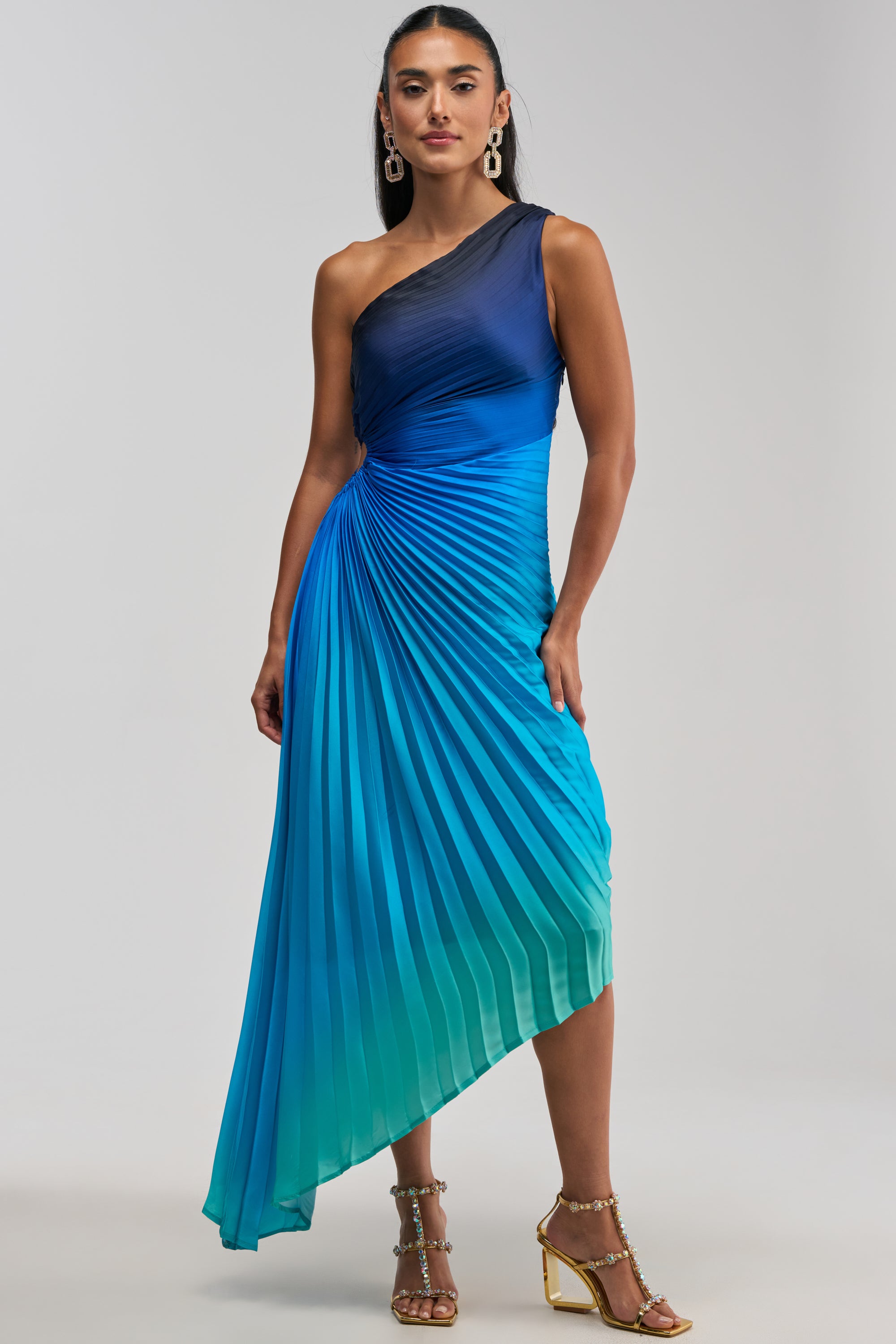 A person wearing the WILD CARD ONE SHOULDER OMBRE MIDI DRESS IN BLUE and gold strappy heels stands against a plain background.