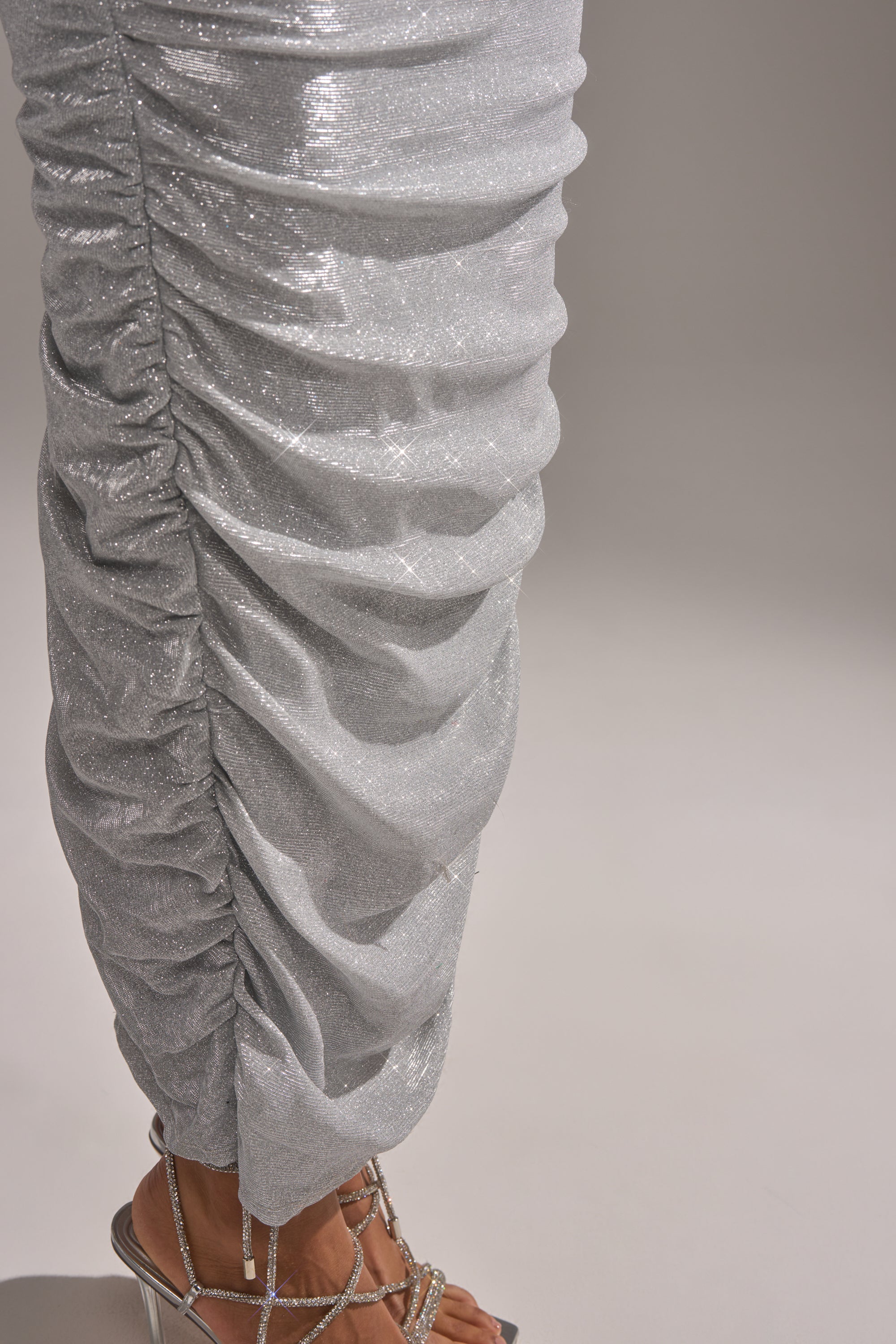 A close-up of a person in silver ruched pants and rhinestone strap heels, perfectly complementing the CANT GET ENOUGH SLINKY RUCHED MAXI DRESS for a truly glamorous look.