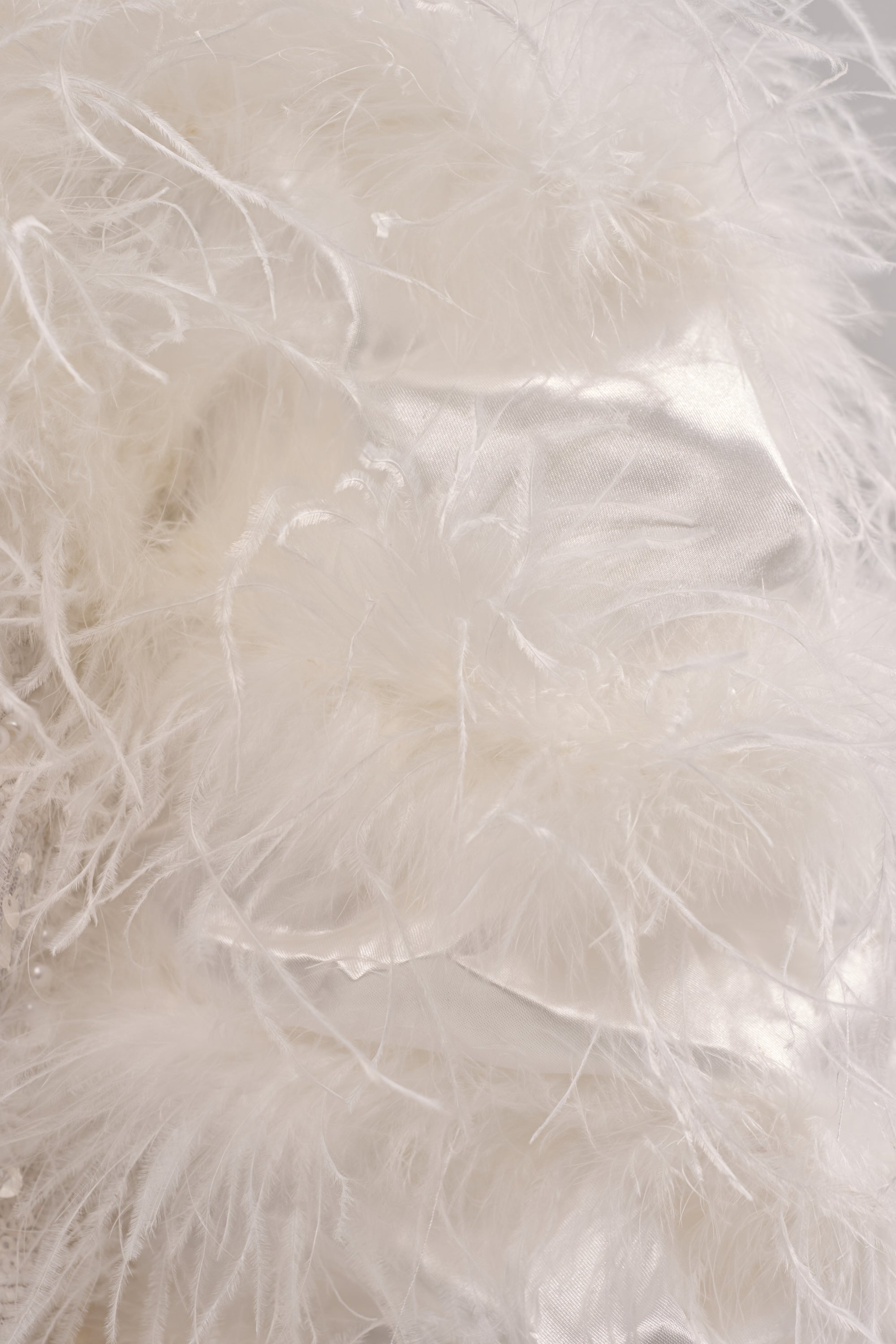 Close-up of soft white feathers merging with smooth, shiny satin fabric, capturing the luxurious and textured elegance of the PARK AVE FEATHER BOLERO.
