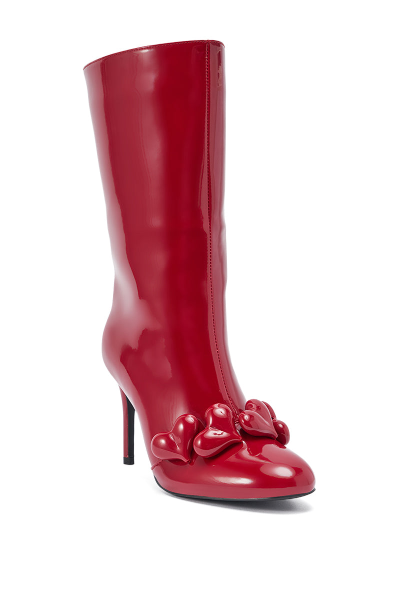 The AZALEA WANG FEDELE Red Patent Heart Embellished Bootie is a shiny, knee-high red patent boot with a stiletto heel, pointed toe, and three sculpted red heart accents on the front near the toe.